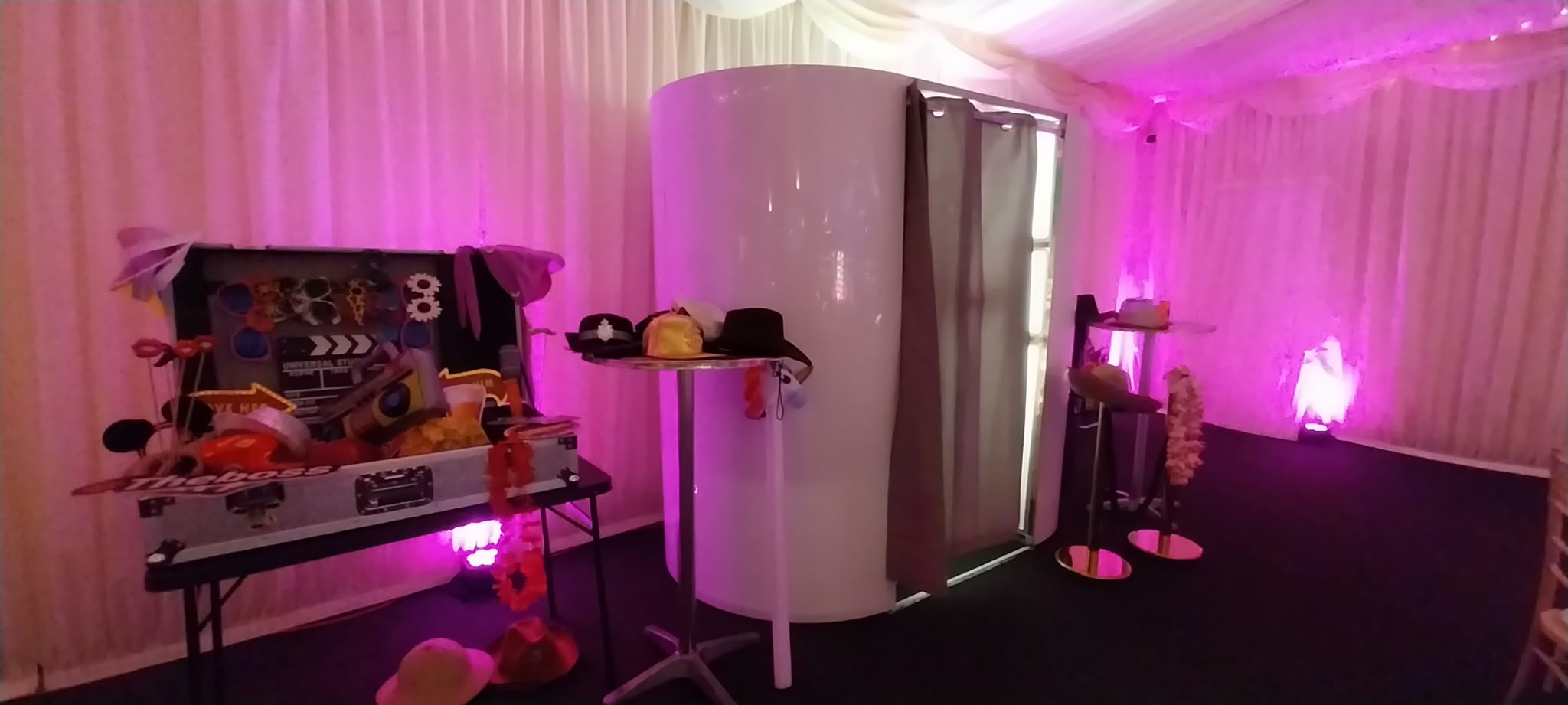Enclosed photo booth with a props table and pink uplighting